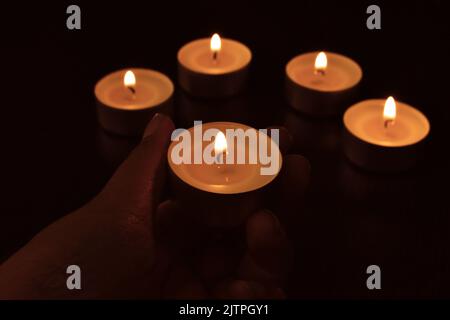 Tea light candles in the dark background.  Hand putting a candle on the table. Stock Photo