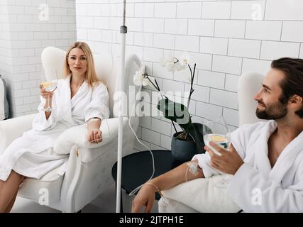 Couple in love during intravenous vitamin therapy. Beautiful woman with her boyfriend with glasses of refreshing drink with lemon in medical clinic fo Stock Photo