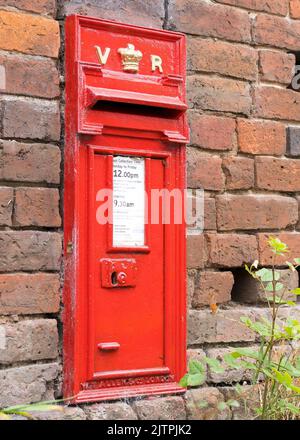 Close up of Victoria Regina red post box set in old brick wall in rural English village. The UK postal service vintage letter boxes still in use today. Stock Photo