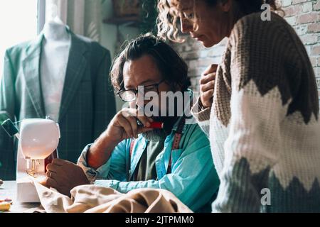Man and woman working together as a team in garment tailor production. Artisan freelance job activity concept. Couple tailoring and working at home or Stock Photo