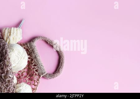 White balls of thread with knitting needles in a string bag on a pink background for knitting warm clothes, hobbies. Overview Stock Photo