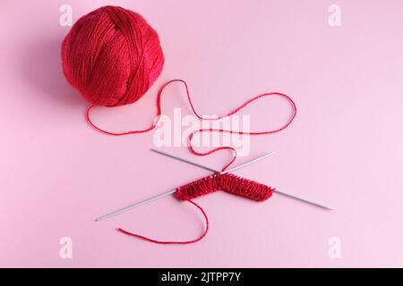 Red knitted wool on a pink background with knitting needles, hobby Stock Photo