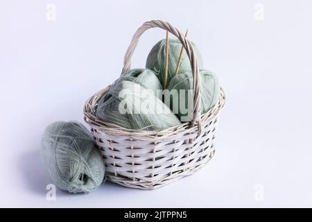 Light green yarn threads in a white basket on a blue background with knitting needles. Stock Photo