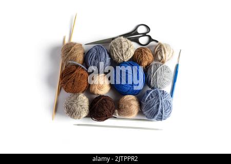 Blue, gray and brown balls of knitting thread with scissors, crochet and knitting needles on a blue background for hobbies. Flat lay Stock Photo