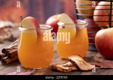 Glass of apple cider with apple slices on wooden table and autumn background Stock Photo