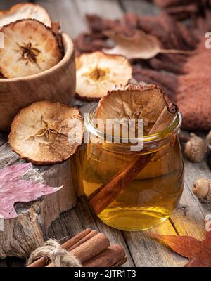 Glass of apple cider with cinnamon stick and dried apple chips on rustic wooden table Stock Photo