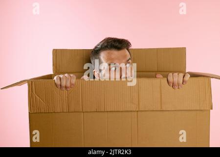 Portrait of funny man peeking out carton box isolated on pink background Stock Photo