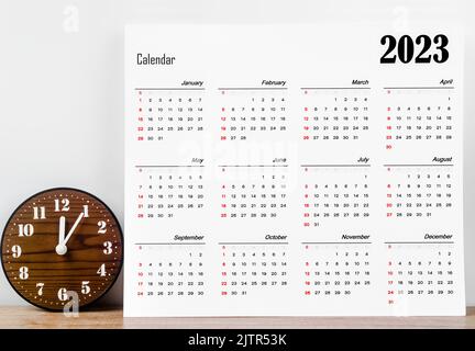 12 months desk calendar 2023 on wooden background with clock. Stock Photo