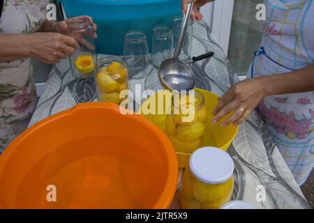 Image of two women preparing canned peaches in jars. Stock Photo