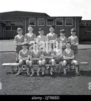 1965, historical, junior school football team group photo. Happy young boys wearing the kit and boots of the era; v- neck shirts, pull-string shorts and football boots, many with leather covered steel toepads including some with a high ankle. Seveal of the boys are wearing the popular 'Gola' boot of the day, a leather football boot, with a lower cut below the ankle, made by Botterill's of Bozeat of Northamptonshire, England, a boot company founded in 1895. In the 1960s, players of the famous Liverpool FC wore Gola football boots. Stock Photo