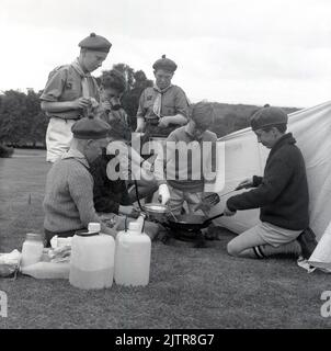 1965, historical, scouting in the Glen, cub scouts in uniform and berets, cooking food in the open-air on the grass ouside a tent, Scotland, UK, looks to be omelettes...... Stock Photo