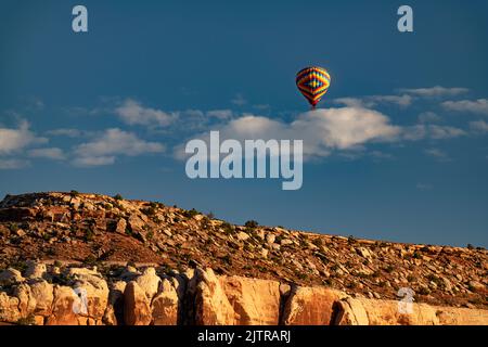 A hot air balloon flies over a mesa along Utah highway 313 in Grand County, Utah Stock Photo