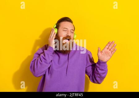 Photo of funny dreamy man wear violet sweatshirt hands earphones singing closed eyes isolated yellow color background Stock Photo