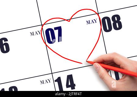 7th day of May. A woman's hand drawing a red heart shape on the calendar date of 7 May. Heart as a symbol of love. Spring month. Day of the year conce Stock Photo