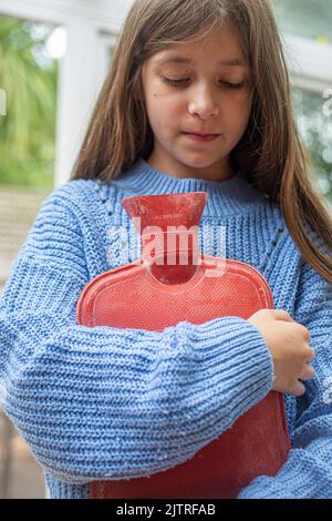 little girl holding hot water bottle against her . Stock Photo