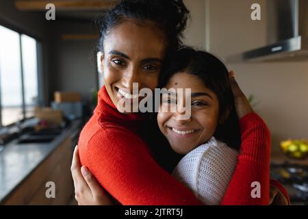 Close-up portrait of smiling biracial mother and daughter hugging in kitchen at home, copy space Stock Photo