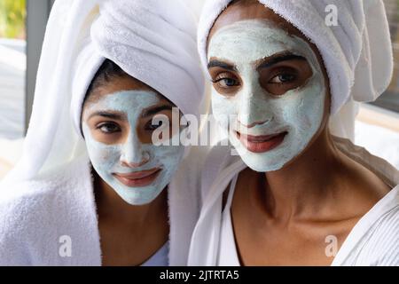 Close-up portrait of biracial mother and daughter with facial masks wearing towels on heads at home Stock Photo