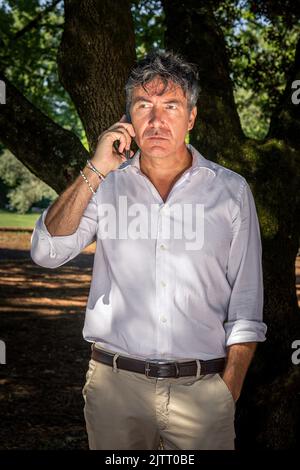 A handsome man with blue eyes wears a white shirt. The businessman is talking on the phone in the park. Stock Photo
