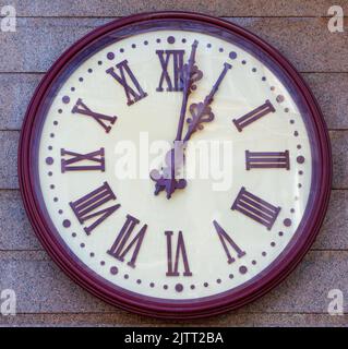 Large outdoor clock on the wall of a red granite building. Stock Photo