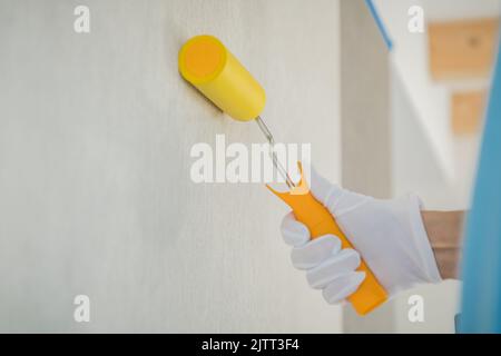 Closeup Photo of Yellow Wallpaper Roller in Worker’s Hand in White Glove Smoothing Out Freshly Pasted Wallpapers. Professional House Renovation Tools Stock Photo