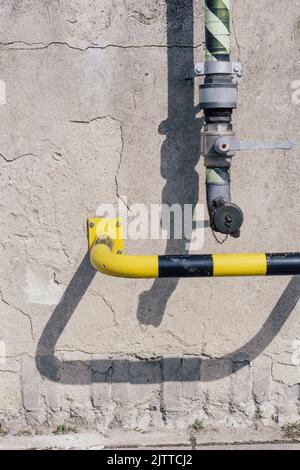 Pipe of a pumping station and safety bar in yellow black on a concrete wall. Stock Photo