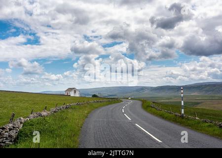 View down the B6277 road towards Middleton-in-Teesdale looking at a painted white stone barn, Weardale, England, UK Stock Photo