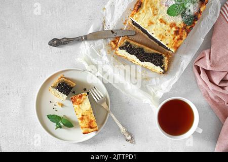 delicious Poppy Seed Cheesecake sliced on a light table, with plates and cup of tea, top view, copy space Stock Photo