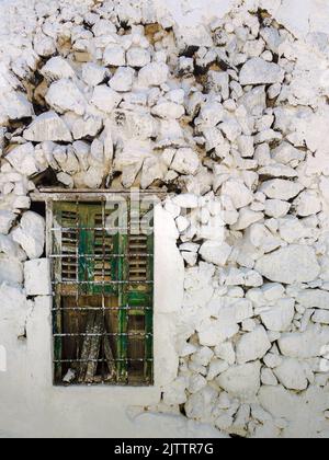 Green broken widnow with fence on a white cracked brick wall Stock Photo