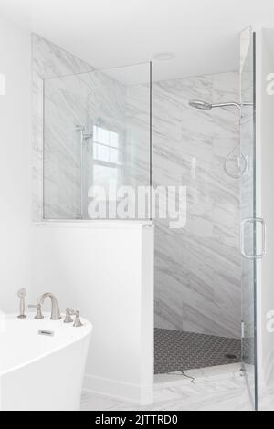 A luxury bathroom shower and freestanding bathtub. The shower is lined with marble tiles and a hexagon tiled floor. Stock Photo