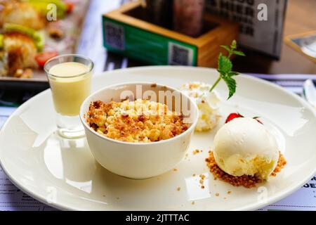 Homemade Apple crumble with vanilla ice cream, strawberry and custard cream on the table Stock Photo