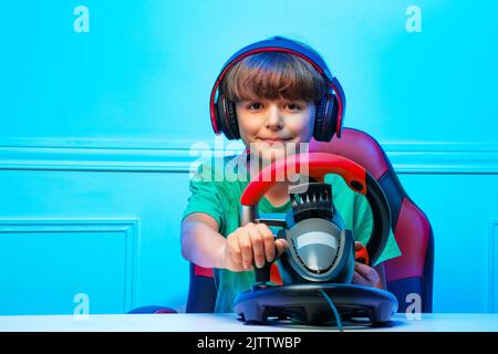 Smiling boy in headphones with steering wheel play race game Stock Photo