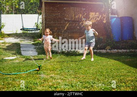 Fun in the garden - children run around water sprinkler Stock Photo