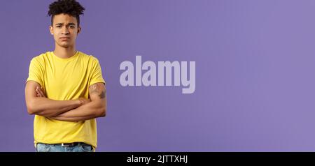 Close-up portrait of skeptical, unimpressed young man with dreads, look judgemental and uninterested, cross arms chest, go on impress me, smirk Stock Photo