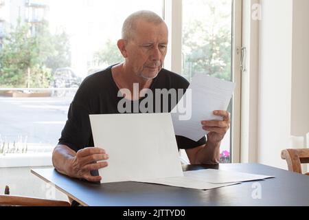 Man reading paper documents while sitting at table. Stock Photo