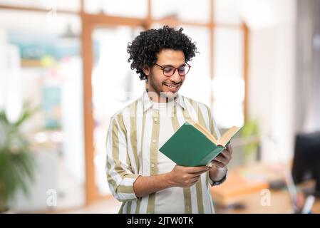 happy young man in glasses reading book at office Stock Photo