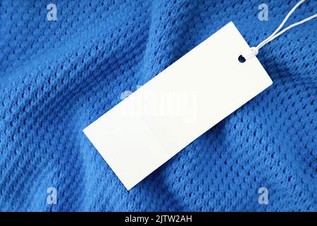 White blank rectangular clothing tag, label mockup template on blue knitted fabric background . Price tag label with copy space for text. Shopping, sa Stock Photo