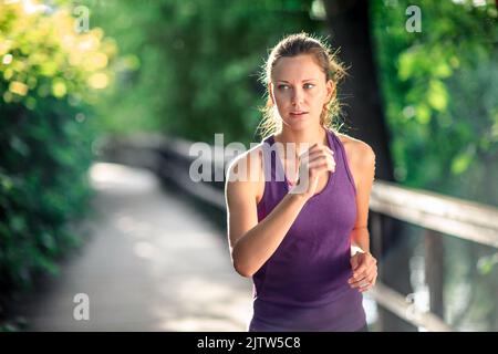 Young healthy athletic woman with fit body running in city nature in the morning. Female model in sportswear exercising outdoors. Copy space. Stock Photo