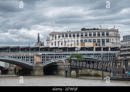 London, England, UK - July 6, 2022: From Thames River. Blackfriars railway bridge landing on north shore under heavy cloudscape. Buildings peep above. Stock Photo