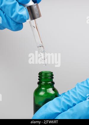 hand hold pipette with medicine oil in a bottle on gray background. Stock Photo