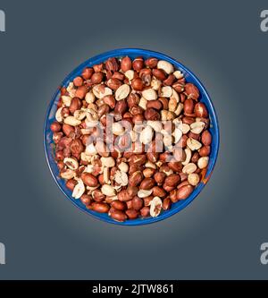 Peeled peanuts for background. Roasted peanut beans with skins. Isolated in a blue plate on a gray gradient. Stock Photo