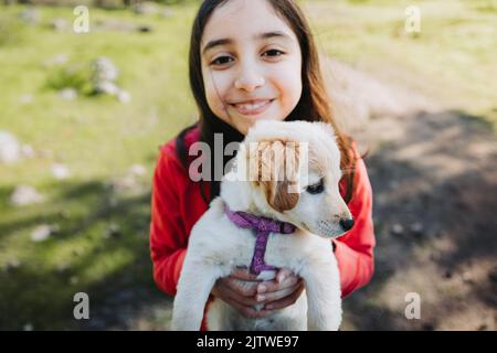 Smiling little girl embracing a golden retriever puppy in the park Stock Photo