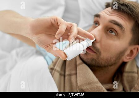 sick man with nasal spray lying in bed Stock Photo