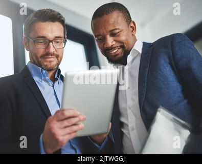 Less paper, more planning. two businessmen using a digital tablet together at work. Stock Photo