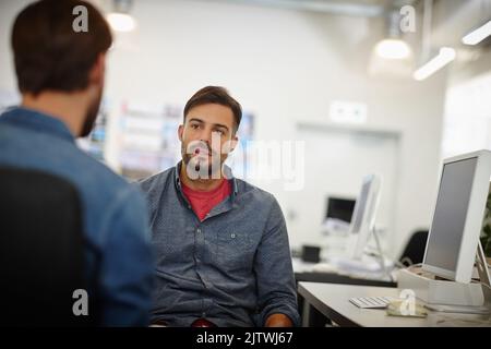Tossing around a few ideas. two young businessmen talking together at a desk in an office. Stock Photo
