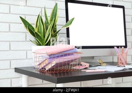 Basket with books, computer and houseplant on table near white brick wall Stock Photo