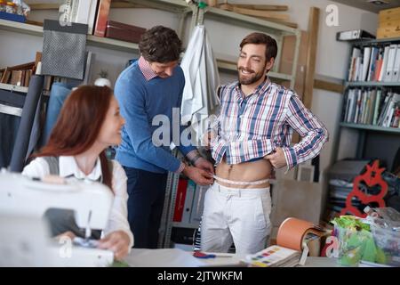 It fits great, thanks. a young fashion designer sewing while a colleague works with a client in the background. Stock Photo