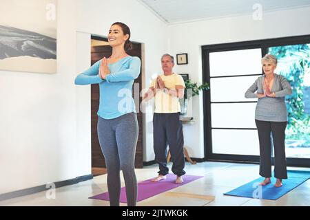 Happiness is lead by healthy habits. a yoga instructor guiding a senior couple in a yoga class. Stock Photo