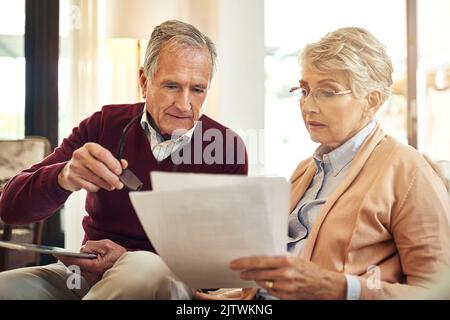 They believe in keeping track of all their expenses. an elderly couple working out a budget while sitting on the living room sofa. Stock Photo