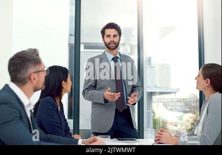 Impressing the team with his brilliant solutions. a businessman giving a presentation to his colleagues in a modern office. Stock Photo