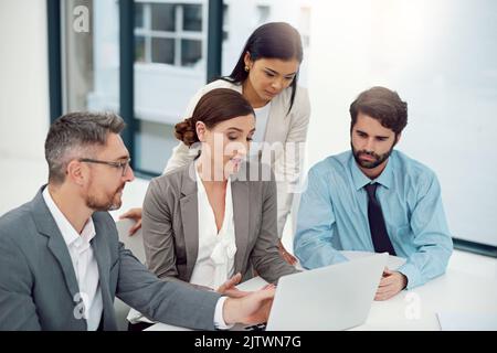 Putting their heads together. a group of businesspeople working together on a laptop in a modern office. Stock Photo